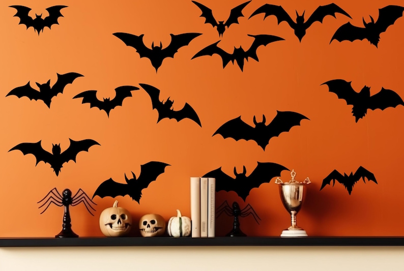 Może przedstawiać: Pomarańczowa ściana ozdobiona czarnymi sylwetkami nietoperzy o r&oacute;żnych rozmiarach. P&oacute;łka prezentuje dekoracje na Halloween, w tym rzeźbione dynie, czaszki i trofeum. Scena wywołuje świąteczną, upiorną atmosferę.