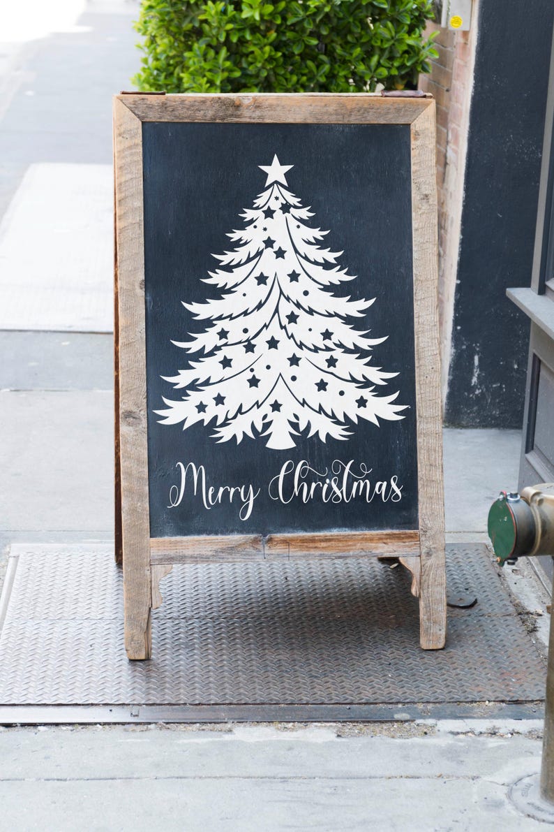 May include: A wooden A-frame chalkboard sign with a white silhouette of a Christmas tree decorated with stars and the text "Merry Christmas".
