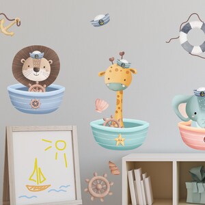 May include: A set of three wall decals featuring a lion, giraffe, and elephant dressed as sailors in boats. The animals are all smiling and have cute expressions. The decals are perfect for a nursery or child's room.