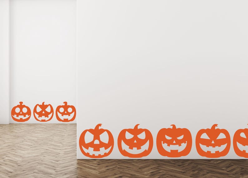 Puede incluir: Adhesivos de pared de calabazas de Halloween naranjas con caras talladas se muestran en una pared blanca. Las calabazas est&aacute;n dispuestas en fila a lo largo de la base de la pared, creando un ambiente festivo y espeluznante.