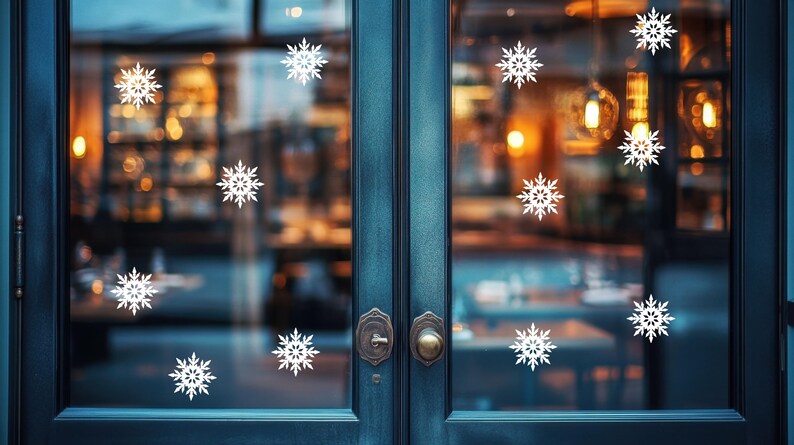 May include: A teal-colored double door with white snowflake decals. The door has ornate hardware and a blurred background of a warmly lit interior. The snowflakes are evenly spaced across the glass panels, creating a festive winter scene.