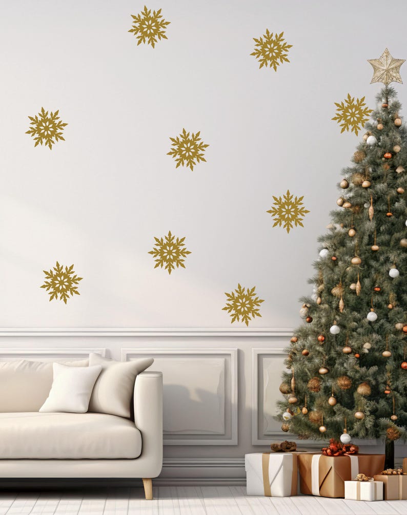 May include: A decorated Christmas tree with gold ornaments and a star topper stands next to a white wall adorned with gold snowflake decals. A white couch and wrapped gifts complete the festive scene.