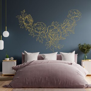 May include: A bedroom with a dark blue wall featuring a gold floral design. The bed has a light pink duvet and white pillows. There are two white nightstands with lamps on either side of the bed.