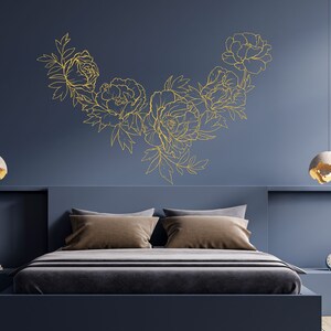 May include: A bedroom with a dark blue wall and a bed with a gold floral design on the wall above the headboard. The bed has a brown headboard and a gray duvet. There are two bedside lamps with white shades.