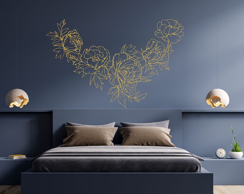 May include: A bedroom with a dark blue wall and a bed with a gold floral design on the wall above the headboard. The bed has a brown headboard and a gray duvet. There are two bedside lamps with white shades.