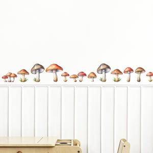 May include: A white wall with a row of watercolor mushroom stickers in various sizes. The mushrooms are red, orange, and brown with white spots. There is a wooden table and chair in the foreground.