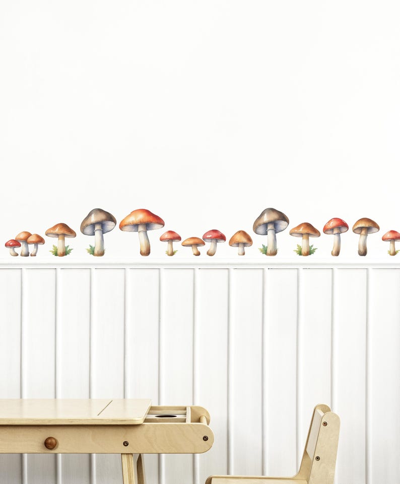May include: A white wall with a row of watercolor mushroom stickers in various sizes. The mushrooms are red, orange, and brown with white spots. There is a wooden table and chair in the foreground.