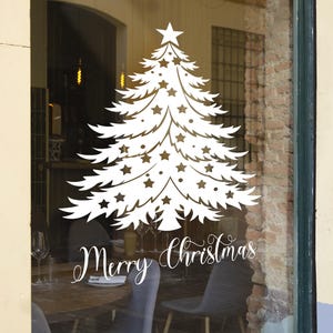 May include: White silhouette of a Christmas tree with stars on a storefront window. The text "Merry Christmas" is written below the tree.