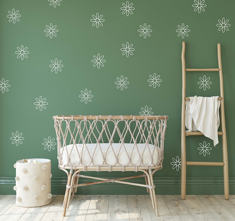 May include: A white wicker crib with a white mattress, a white pom-pom storage bin, and a wooden ladder leaning against a green wall with white daisy decals.