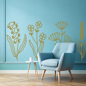 May include: A light blue armchair with wooden legs sits in front of a wall with gold floral decals. The wall is painted a light blue color.