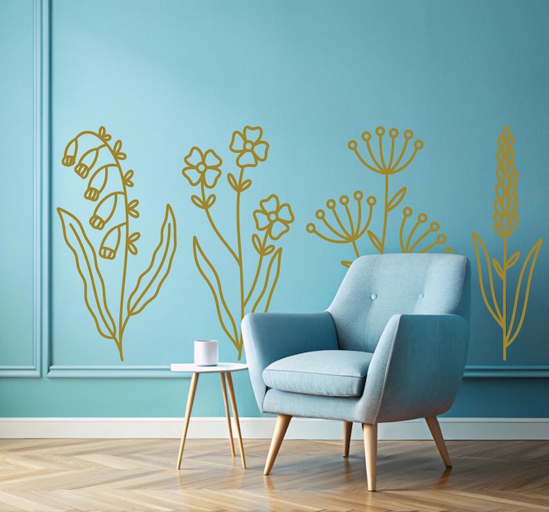 May include: A light blue armchair with wooden legs sits in front of a wall with gold floral decals. The wall is painted a light blue color.