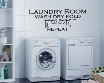 May include: A white laundry room with a washing machine and dryer. The wall has a black vinyl decal that reads "Laundry Room Wash Dry Fold Repeat" with a clothesline and clothes hanging on it.