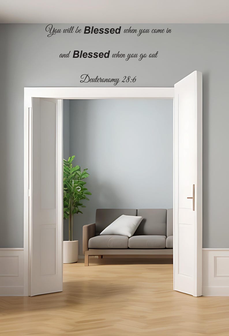 Pu&ograve; includere: Una porta bianca con una maniglia nera &egrave; aperta per rivelare un soggiorno con un divano grigio, una pianta verde e un pavimento in legno. La parete dietro la porta ha una citazione di testo nero che recita "You will be Blessed when you come in and Blessed when you go out Deuteronomy 28:6".
