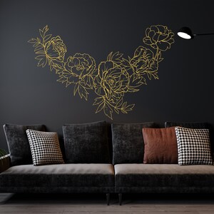 May include: A black couch with three pillows, two black and white patterned pillows and one brown pillow, in front of a black wall with a gold floral design.