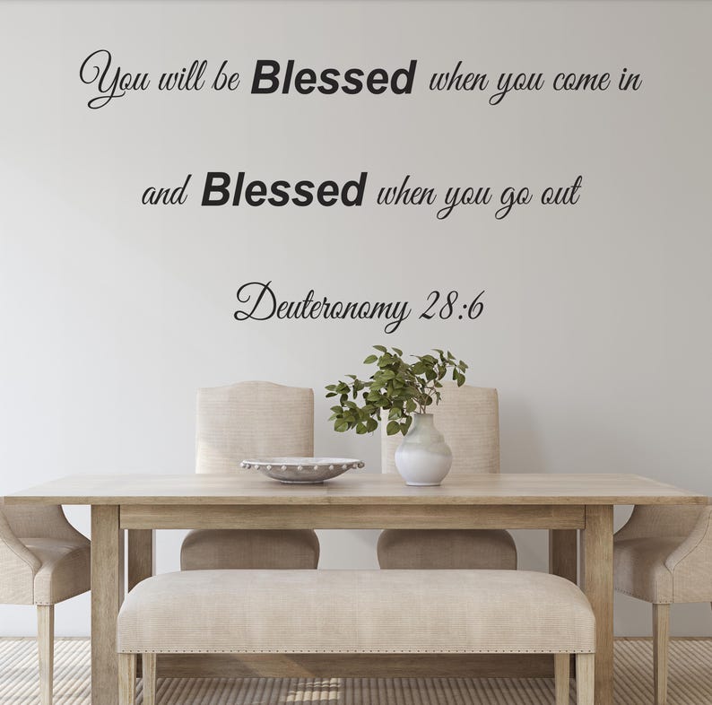Pu&ograve; includere: Un adesivo da parete con la citazione "You will be Blessed when you come in and Blessed when you go out Deuteronomy 28:6" in corsivo nero. L'adesivo &egrave; esposto su una parete bianca sopra un tavolo da pranzo in legno con due sedie e una panca.