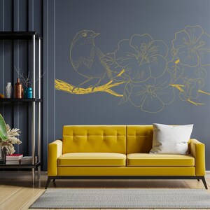 May include: A yellow sofa with a white pillow sits in front of a gray wall with a gold bird and flower design.