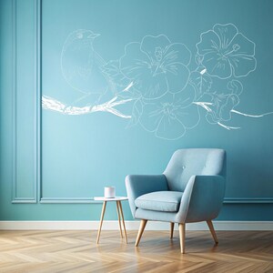 May include: A light blue armchair with wooden legs sits in front of a light blue wall with a white floral design and a white bird. A small table with a white cup sits in front of the chair.