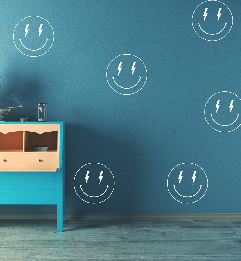 May include: A teal blue dresser with two drawers and a light wood top against a blue wall with white lightning bolt smiley face decals.