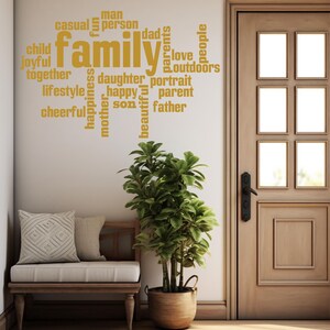 May include: A gold vinyl wall decal with the word "family" in large letters surrounded by smaller words like "love", "joyful", "happy", "together", "parents", "daughter", "son", "father", "mother", "casual", "person", "lifestyle", "cheerful", "beautiful", "portrait", "outdoors", "people", "man", "dad", "fun", "child", "parent".