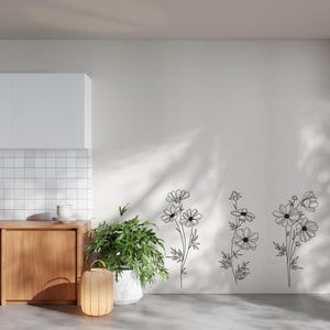 K&ouml;nnte beinhalten: Eine wei&szlig;e Wand mit drei schwarzen Linienzeichnungen von Kosmosblumen. Die Blumen sind in einem einfachen, minimalistischen Stil gehalten.