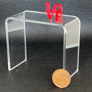 Könnte beinhalten: Ein durchsichtiger Acryl-Präsentationsständer mit einem roten LOVE-Schild obenauf. Der Ständer ist etwa 12,5 cm hoch und 10 cm breit. Eine 50-Cent-Euro-Münze befindet sich im Vordergrund zur Größenbestimmung.