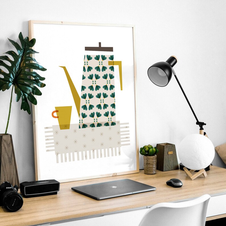 May include: A framed print of a stylised illustration of a green and white patterned coffee pot with a yellow spout, a yellow cup, and a white and gold patterned rug. The print is on a white background and is framed in a light wood frame.