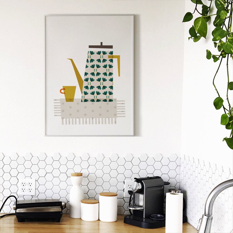 May include: A framed print of a green and white patterned coffee pot with a yellow spout and a yellow cup on a white and grey patterned table runner. The print is on a white wall with white hexagonal tiles below.