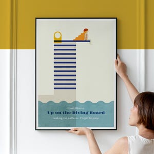 Op de afbeelding: Een ingelijste kunstdruk met een gestileerde afbeelding van een persoon met lang oranje haar die op een hoge, blauw-wit gestreepte duikplank boven blauwe golven zit. De tekst luidt Ocean Observer, Up on the Diving Board, Looking for patterns. Forgot to jump.