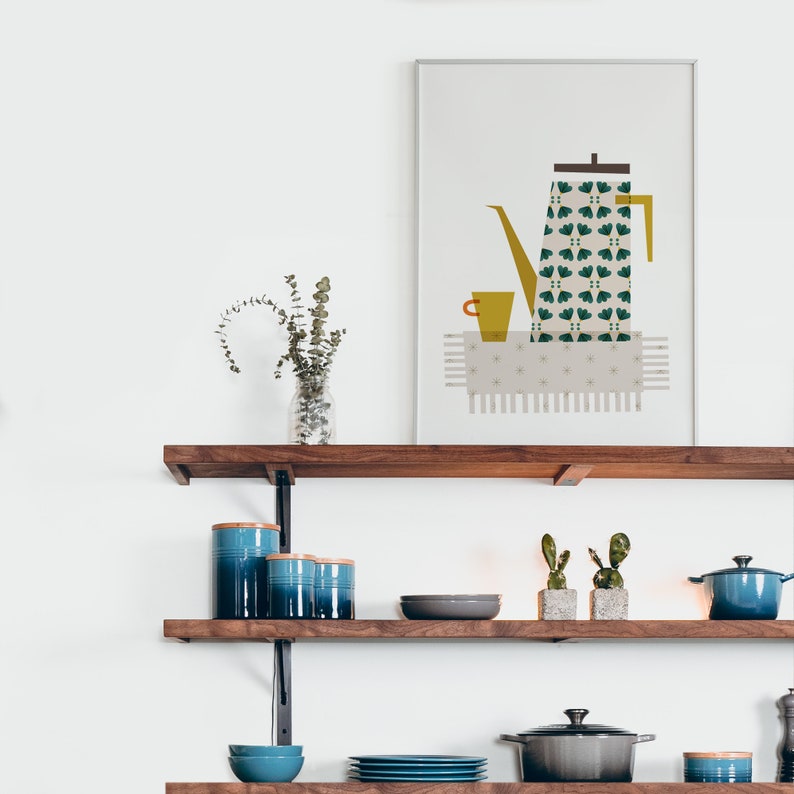 May include: A framed print of a stylised illustration of a green and yellow coffee pot with a cup on a white background. The print is hanging on a wall above a wooden shelf with blue ceramic canisters, a grey bowl, and a green cactus.