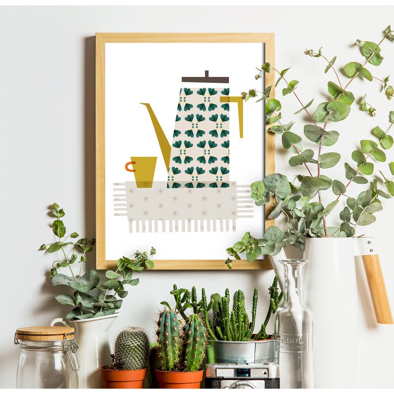 May include: A framed print of a stylised illustration of a green and white patterned coffee pot, a yellow cup, and a white tablecloth with a fringe. The print is in a wooden frame.