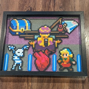 以下が含まれることがあります： ビデオゲームのシーンを描いた、額縁に入ったピクセルアート作品。シーンには、赤いハート、スケルトン、青いチェスト、王冠をかぶったキャラクター、剣を持ったキャラクターが描かれている。背景は、紫と青のピクセル模様である。