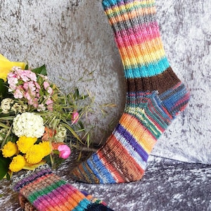 Könnte beinhalten: Ein Paar handgestrickte Socken mit einem lebendigen, mehrfarbigen Streifenmuster in Rosa, Orange, Gelb, Türkis, Blau und Braun. Die Socken verfügen über ein geripptes Bündchen und eine verstärkte Fersenkonstruktion aus meliertem Garn.