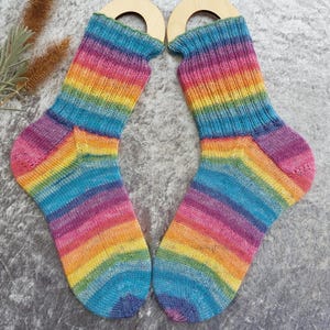 May include: A pair of rainbow-striped socks, featuring a vibrant spectrum of colors including blue, purple, yellow, and orange. The socks are made of a knitted material and are displayed on wooden sock forms. The socks are designed for comfort and style.