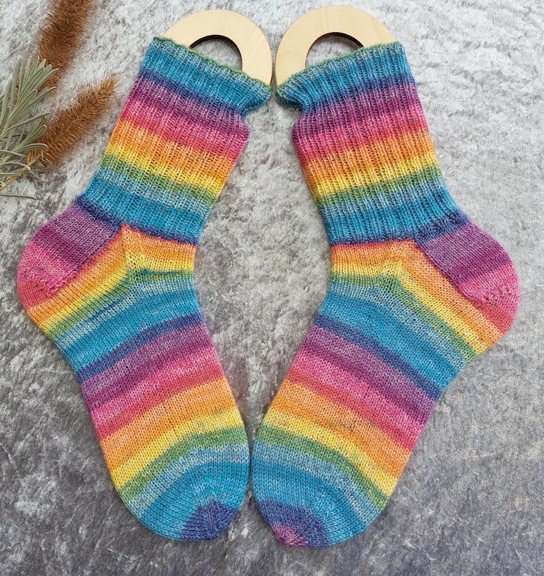 May include: A pair of rainbow-striped socks, featuring a vibrant spectrum of colors including blue, purple, yellow, and orange. The socks are made of a knitted material and are displayed on wooden sock forms. The socks are designed for comfort and style.