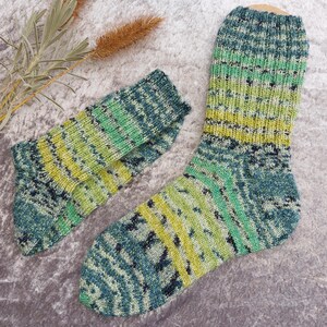 May include: A pair of hand-knitted socks in shades of green, blue, and yellow. The socks have a textured pattern and are displayed on a gray surface. The color gradient creates a visually appealing design, perfect for cozy wear.