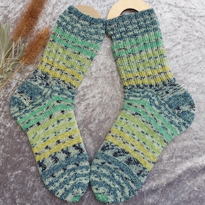 May include: A pair of hand-knitted socks in shades of blue, green, and yellow. The socks feature a ribbed design on the upper portion and a patterned design on the foot. The socks are displayed on wooden sock forms.
