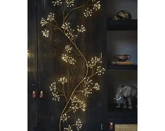 Puede incluir: Una lámpara vertical y flexible en forma de rama, con múltiples tallos delgados de color marrón que se ramifican en grupos de pequeñas luces LED de color blanco cálido, creando una estructura botánica iluminada.