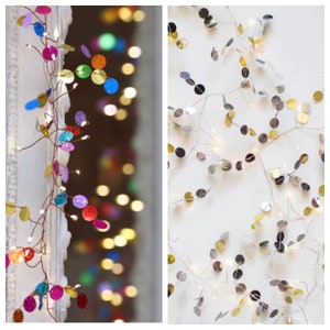 May include: Two strands of fairy lights with round, colourful, glittery ornaments. The lights are strung on a copper wire. One strand has silver ornaments and the other has multi-coloured ornaments.