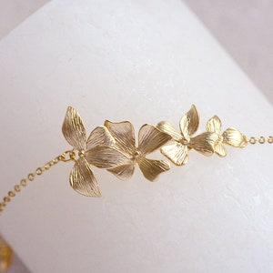 Pode incluir: Um bracelete de corrente dourada com um delicado design floral. O bracelete apresenta v&aacute;rias flores pequenas, intrincadamente detalhadas, conectadas por uma corrente fina.