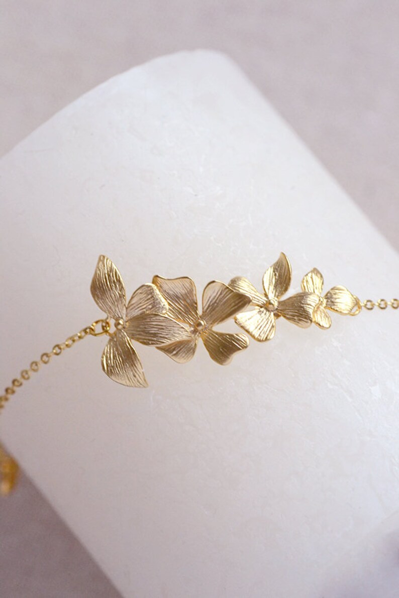 Pode incluir: Um bracelete de corrente dourada com um delicado design floral. O bracelete apresenta v&aacute;rias flores pequenas, intrincadamente detalhadas, conectadas por uma corrente fina.