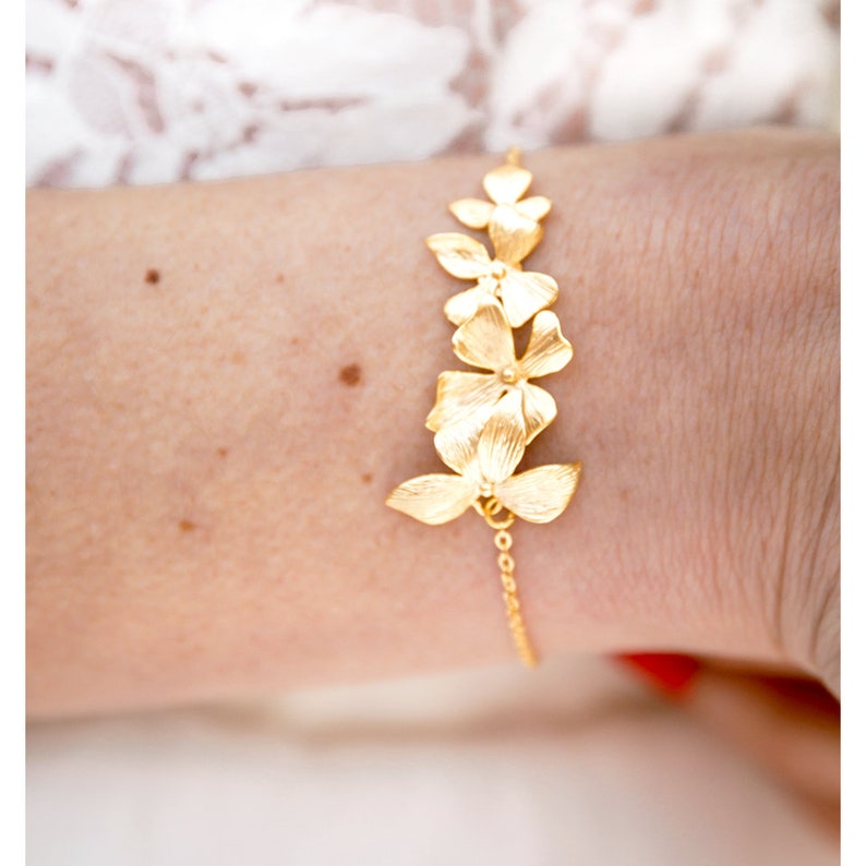 Pode incluir: Um bracelete de ouro com uma corrente delicada e um design de cinco flores douradas.