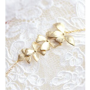 Pode incluir: Um bracelete dourado com uma corrente delicada e uma s&eacute;rie de pingentes em forma de flor. As flores est&atilde;o dispostas em cascata, com a maior flor no topo e a menor flor na parte inferior.