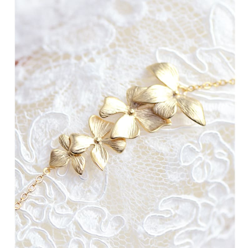 Pode incluir: Um bracelete dourado com uma corrente delicada e uma s&eacute;rie de pingentes em forma de flor. As flores est&atilde;o dispostas em cascata, com a maior flor no topo e a menor flor na parte inferior.