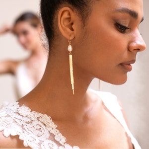 Peut inclure: Une femme portant un haut en dentelle blanche avec une boucle d'oreille en chaîne dorée ornée d'une perle.