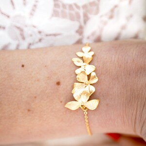 Pode incluir: Um bracelete de ouro com uma corrente delicada e um design de cinco flores douradas.