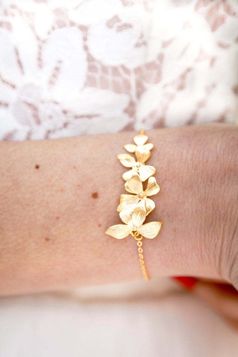 Pode incluir: Um bracelete de ouro com uma corrente delicada e um design de cinco flores douradas.