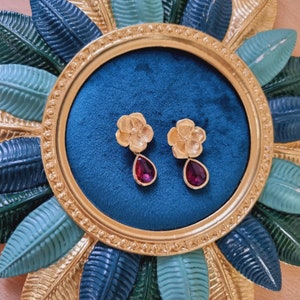Op de afbeelding: Een paar gouden oorbellen met een bloemmotief en een traanvormige rode edelsteen.