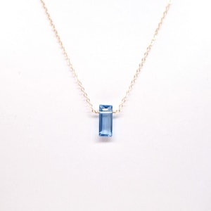 May include: A delicate gold chain necklace with a light blue rectangular gemstone pendant.
