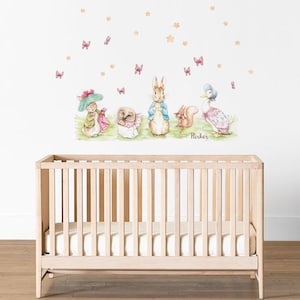Puede incluir: Una pared blanca con una calcomanía de pared con temática de guardería que presenta a Peter Rabbit y sus amigos. La calcomanía incluye un conejo, un erizo, una ardilla, un pato y mariposas. El nombre "Parker" está escrito debajo de los personajes. Una cuna de madera está en primer plano.