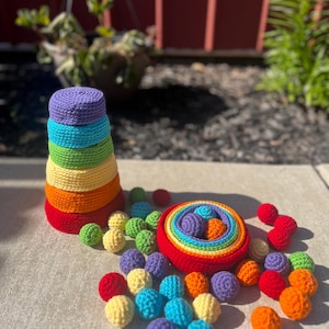 May include: A rainbow-colored crocheted stacking toy with a set of colorful crocheted balls. The toy is made of soft yarn and is perfect for babies and toddlers.